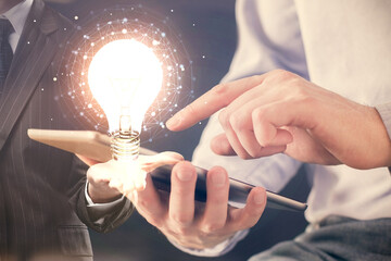 Double exposure of man's hands holding and using a digital device and bulb hologram drawing. Idea concept.