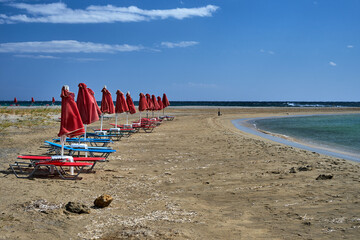 Umbrellas and beach beds on a windy day on the sandy coast of Crete island