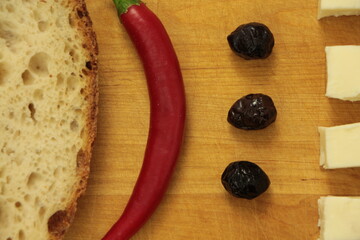 Obraz na płótnie Canvas Close up the black olives, feta cheese, red pepper and a slice of sourdough bread on the wooden cutting board. Breakfast. Healthy foods