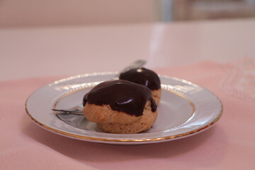 Homemade profiteroles covered with chocolate sauce on the pink tablecloth. Profiterole choux with chocolate ganache on the plate. Delicious eclair dessert with cream and chocolate glaze. 