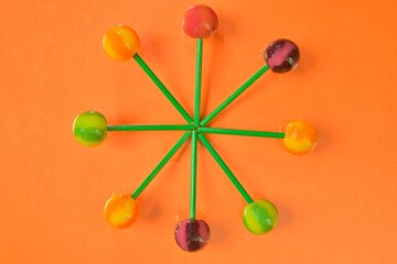 Colorful lollipops on green sticks in round. Multicolored candies on orange background, top view. Summer and pop art concept. Flat lay. Real reflection