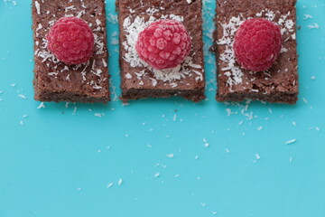 Raspberry and coconut zest on three pieces of chocolate cake. Blue background. Top view. Brownie