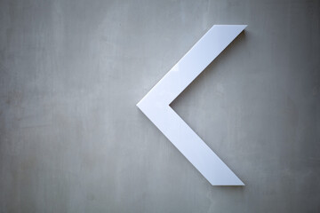 focus on the white arrow that is made of plastic, pointing left is placed on an empty cement wall space background