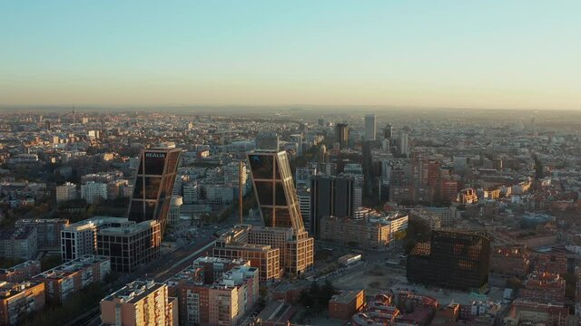 Forwards fly above business district of city in evening sunlight. Leaned office twin towers at Plaza de Castilla square.
