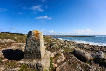 Boundary stone on the Breton coast. Landscape with sea water against blue sky. Rocky background. France, Brittany, Audierne, Lervily.