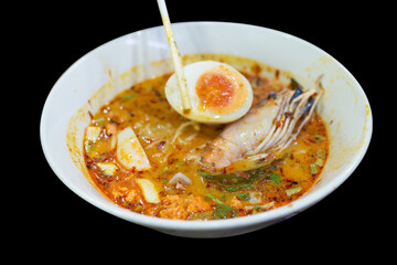 Die cut of Tom Yum Goong spicy shrimp soup with Thai spices on black background.