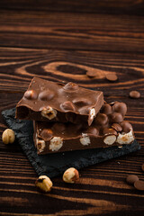 Delicious milk chocolate bars with nuts close up. Stack of chocolate slices Hazelnut pieces tower. Sweet food photo concept