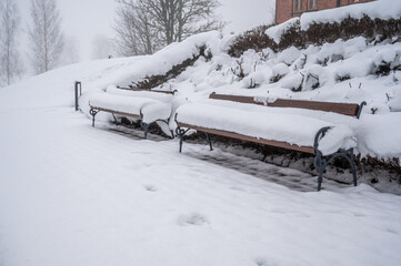 Snow-covered wooden benches in a city park. Snowy winter in Europe.
