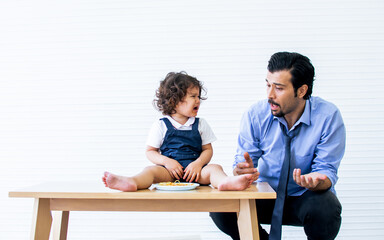 Caucasian beard handsome father trying to taking care and giving his little cute daughter spaghetti...