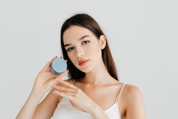 Photo of attractive woman with perfect makeup posing with blue jar of skin cream product, looking at the camera. Cosmetologist recommendation