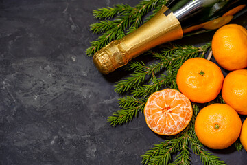 Christmas composition with tangerines and champagne on black background, with green spruce tree branch. Flat lay