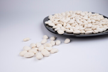 White haricot on a black plate and on a white background. Beans scattered over white background