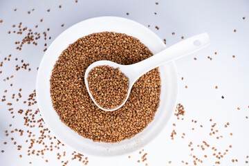 Buckwheat on white background. Plate with buckwheat and a spoon on white background. Buying buckwheat. Healthy food