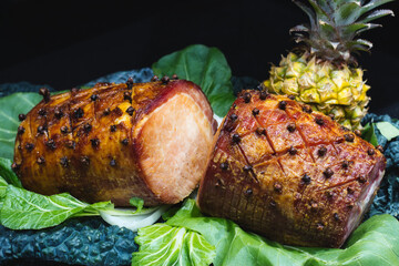 Cooked gammon joint with whole pineapple against a black background