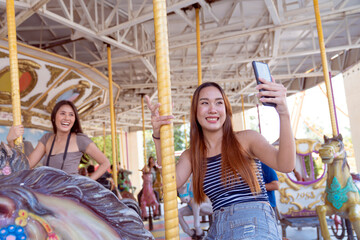 Lesbian Concept. Young pretty woman taking selfie on carousel in amusement park. Attractive two women taking selfie in amusement park.