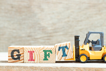 Toy forklift hold letter block t in word gift on wood background