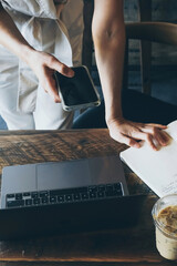Young business woman standing by table, using mobile phone and checking email. Freelance concept. Female works in dark interior  cafe. Student checking schedule.
