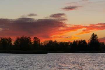 Fototapeta na wymiar Orange red clouds after sunset over trees and lake