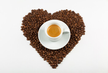 Heart shape made from coffee beans and a cup of cappuccino coffee on a white background. Flat lay. Coffee love concept