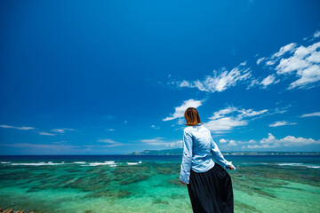 沖縄の青い海を立って見つめる女性