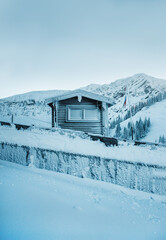 Small wooden house in spruce trees forest in Bayern Alps, Germany. Winter landscape with snow and clouds. Cold day.