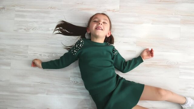 A preschool-age girl is lying on the floor, spinning on her back and laughing