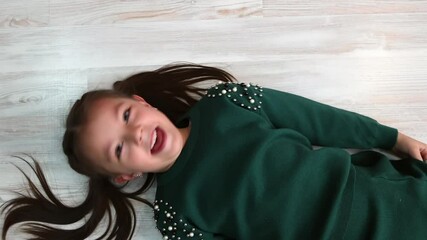 A preschool-age girl is lying on the floor and laughing