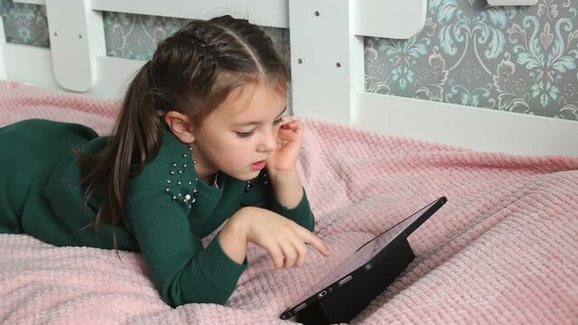 A preschool girl looks at pictures on an electronic tablet