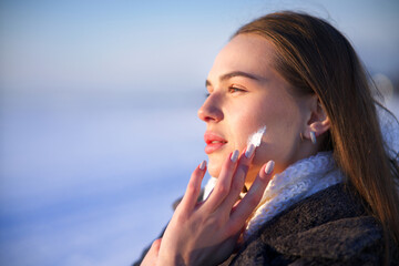 Portrait of beautiful woman applying cosmetic skin cream on face and hands, protecting from cold...