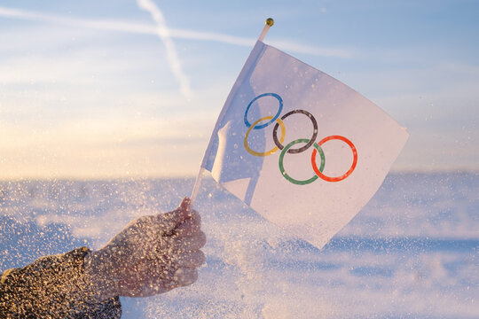 The Olympic flag, small in hand, flutters against the backdrop of snow and trees Concept for Winter Olympic Games 2022.