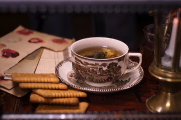 Holiday evening at home - porcelain cup of best herbal tea, antique candle in candlestick, old letters and jar of honey
