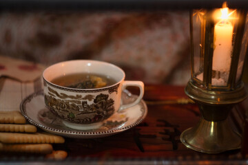 Holiday evening at home - porcelain cup of best herbal tea, antique candle in candlestick, old letters and jar of honey