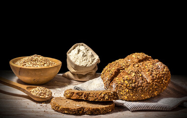 Loaf of cereal bread on wooden table and dark background. Wooden spoon and bowl decoration with flour and multigrain