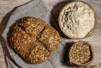 Loaf of cereal bread on wooden table and dark background. Wooden spoon and bowl decoration with flour and multigrain