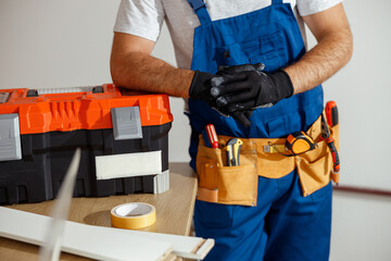 Cropped shot of technician in uniform and protective gloves posing for camera indoors, leaning on a toolbox