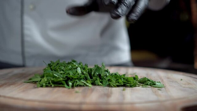 A chef in black gloves chops parsley on wooden cut board