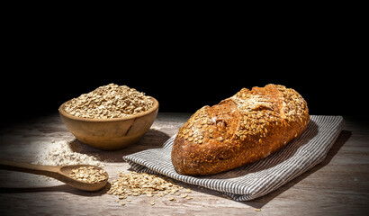 Still life of oat bread. Oat bread on black background on wooden table, with wooden bowl full of flour and wooden spoon with rolled oats