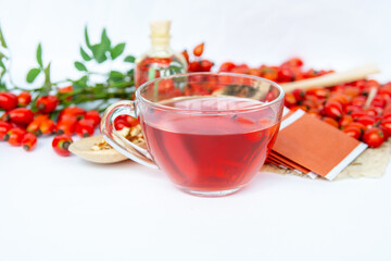 Dog rose, bunch branch Rosehips, types Rosa canina hips, essential oil and hot herbal tea cup on white background. Medicinal plants and herbs composition