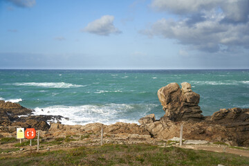 Rocks at the water's edge from the beach. Cloudy sky in sunlight. Well known surf spot in La Torche in Brittany near Plomeur.
