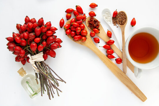 Dog rose, bunch branch Rosehips, types Rosa canina hips, essential oil and hot herbal tea cup on white background. Medicinal plants and herbs composition