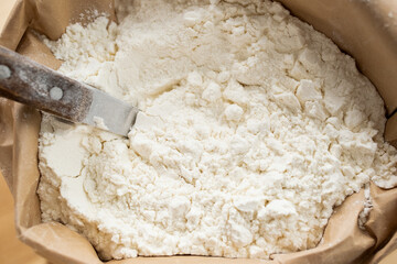 Overview of pile of fresh wheat flour in eco-friendly paper sack and spoon for taking it out