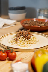 Heap of appetizing served boiled spaghetti with fried minced meat on top standing on wooden table in the kitchen