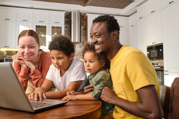 Cheerful family members in casualwear looking at laptop screen while communicating with friends in video chat