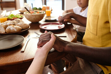 Hands of African man, his Caucasian wife and their son during pray by table before having dinner or breakfast