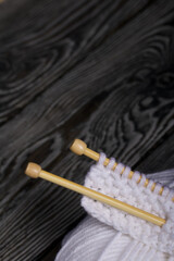 Knitting with wooden needles. A skein of white thread and a fragment of a knitted product. On black pine boards. Close-up.