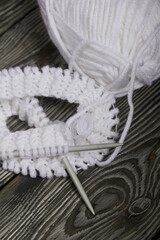 Knitting with needles. A skein of white thread and a fragment of a knitted product. On black pine boards. Close-up.