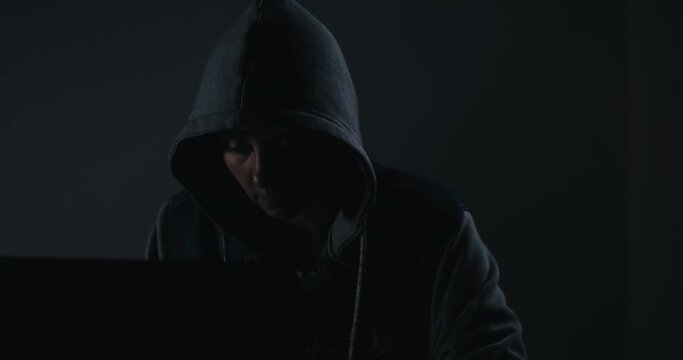 woman wearing hood on looking dark and dangerous hacking laptop computer system on black background in cybercrime or cyber crime and internet. criminal concept.