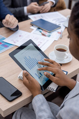 Hand of young African businesswoman scrolling in tablet with charts and diagram on screen while sitting by table