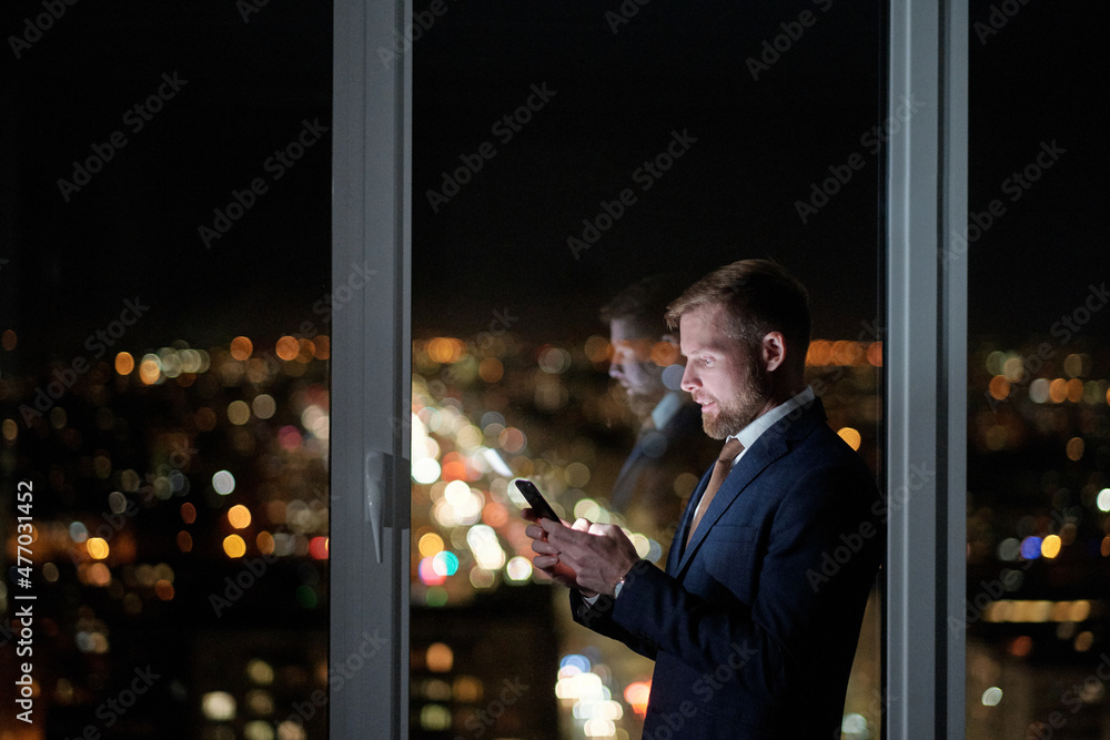 Poster side view of businessman in formalwear scrolling in mobile phone against large office window while w