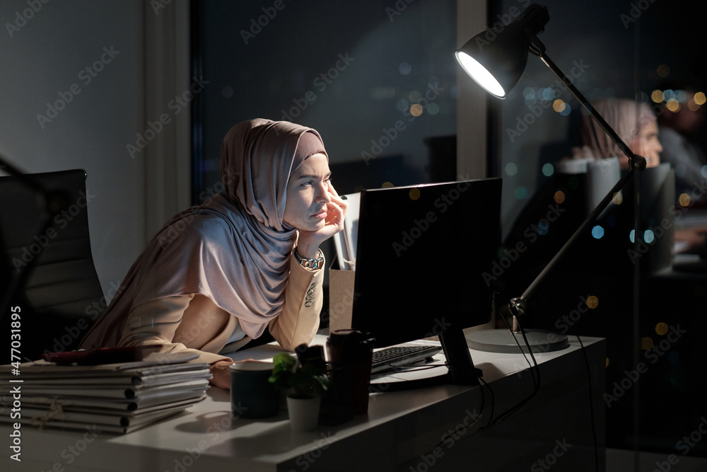 Poster contemporary female office worker looking at data on computer screen while sitting in front of monit